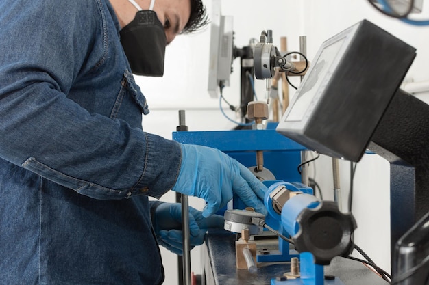 Primer plano de un hombre latino usando máscara protectora y guantes de látex azul calibrando una máquina de prueba geológica