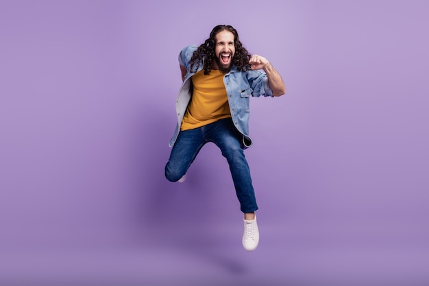 Primer plano de hombre loco saltar volar correr usar ropa casual en la pared púrpura