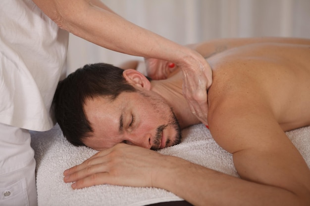 Primer plano de un hombre maduro relajándose en el spa, recibiendo un masaje profesional de tejido profundo