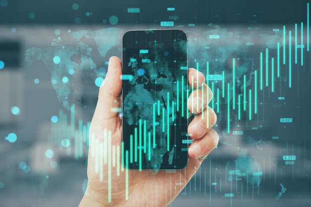 Primer plano de un hombre con la mano sosteniendo un teléfono móvil con gráfico de divisas azul en crecimiento y holograma de mapa en el fondo borroso del interior de la oficina Concepto de inversión bancaria y crecimiento financiero Exposición doble