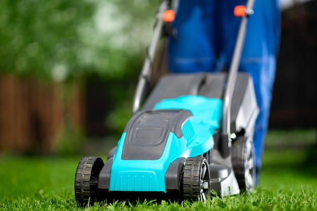 Primer plano de un hombre con un mono con una cortadora de césped cortando césped verde en un jardín moderno.