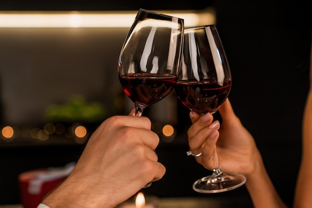 Primer plano de hombre y mujer brindando y bebiendo vino tinto de copas en la cena