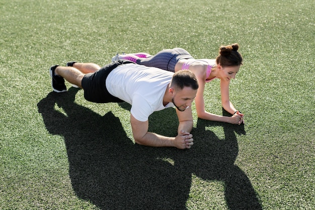 Foto primer plano de un hombre y una mujer haciendo un ejercicio de tabla sobre el césped en un estadio deportivo al atardecer