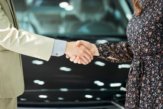 Primer plano de un hombre y una mujer de pie y dándose la mano después del trato en el salón del automóvil