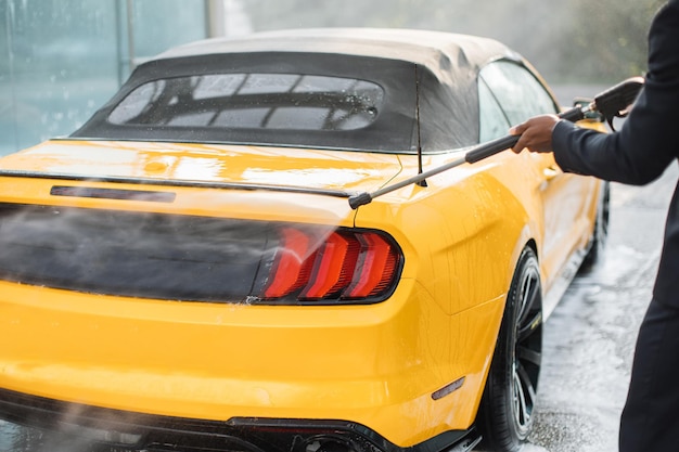 Primer plano de un hombre de negocios africano limpiando los faros traseros de su automóvil amarillo de lujo