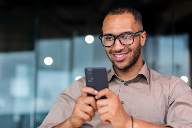 Primer plano de un hombre de negocios afroamericano sonriente usando mensajes de escritura de teléfono y navegando por Internet