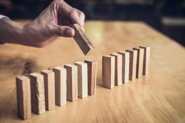 Primer plano de un hombre de negocios jugando con la mano colocando un bloque de madera en una línea de dominó Riesgo y estrategia en los negocios