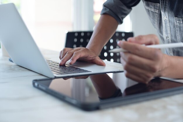 Primer plano de un hombre de negocios trabajando en una computadora portátil navegando por Internet y usando una tableta digital en la mesa de la oficina