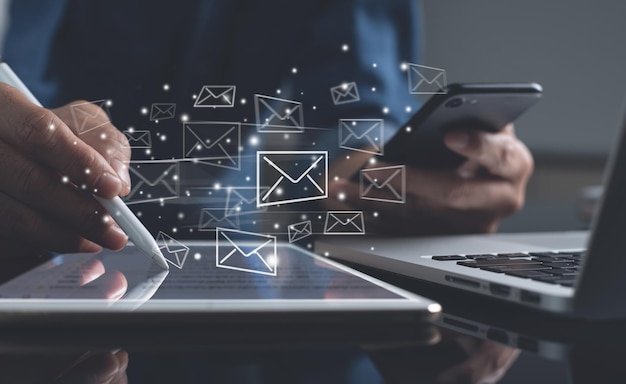 Un primer plano de un hombre de negocios trabajando en la oficina usando una tableta digital y un teléfono inteligente móvil con iconos de correo electrónico en una pantalla virtual.