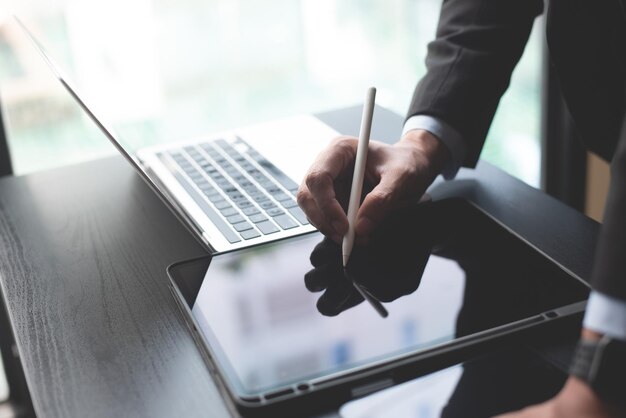 Primer plano de un hombre de negocios usando un lápiz estilográfico firmando un documento en una tableta digital y trabajando en una computadora portátil comprobando un documento digital firmando una firma electrónica