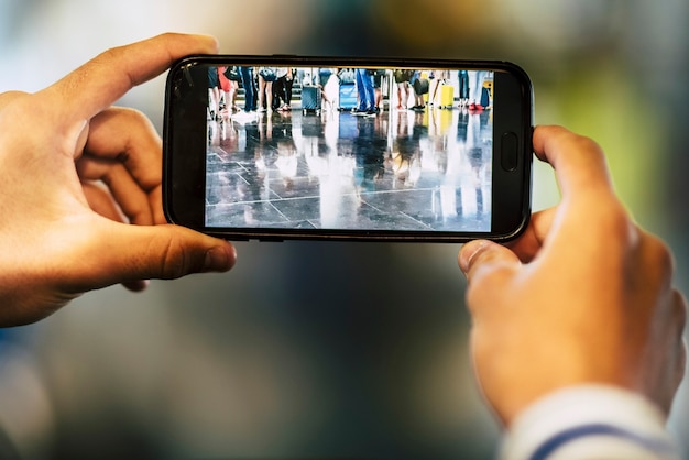 Primer plano de un hombre o una mujer tomando una fotografía de las piernas de un gran grupo de personas esperando para entrar en su vuelo en el aeropuerto