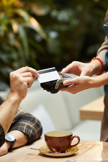 Foto primer plano del hombre pagando la taza de café con tarjeta de crédito al camarero en el restaurante