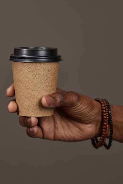 Primer plano del hombre que sostiene la taza desechable con café en la mano aislado en la pared gris