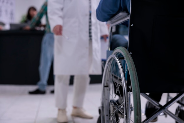 Primer plano de un hombre que usa silla de ruedas frente a un médico en la recepción de un hospital privado para un chequeo de rutina. Enfoque selectivo en el hombre mayor que vive con discapacidad en la recepción de la clínica para la cita.