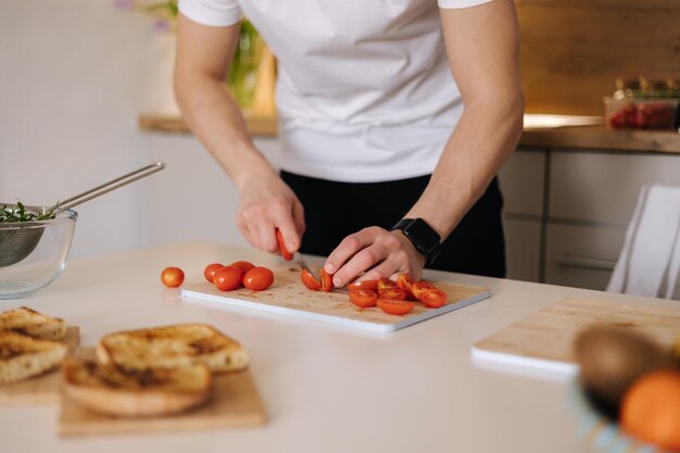 Primer plano de hombre rebanada pequeños tomates orgánicos en tablero de madera Tomate cherry rojo