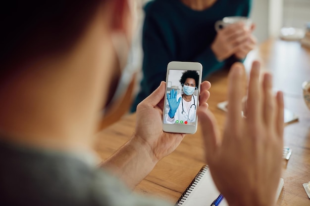 Primer plano de un hombre saludando a su médico durante una videollamada por teléfono inteligente