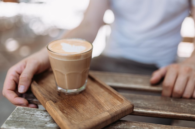 Primer plano de un hombre sentado en una mesa de madera al aire libre con una taza de café recién hecho caliente Persona del sexo masculino disfrutando de una bebida matutina al aire libre