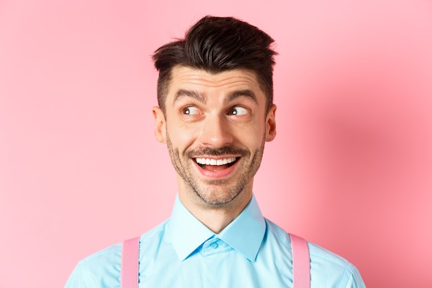 Primer plano de hombre sonriente alegre, mirando a un lado en el logotipo, mirar el trato promocional con cara emocionada, de pie sobre fondo rosa.