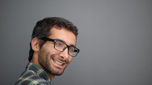 Primer plano de un hombre sonriente con anteojos sobre un fondo gris