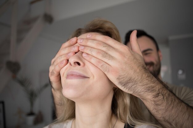 Foto primer plano de un hombre sonriente cubriendo los ojos de su novia en casa.