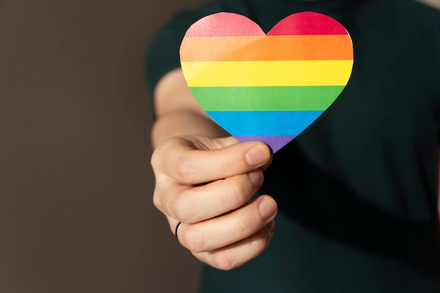 Primer plano de un hombre sosteniendo un corazón de papel colores de la bandera LGBT concepto de amor gay