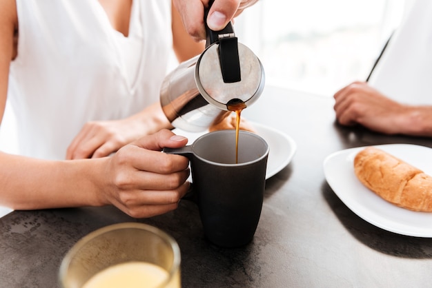 Primer plano del hombre vertiendo café en la taza de su novia en la cocina