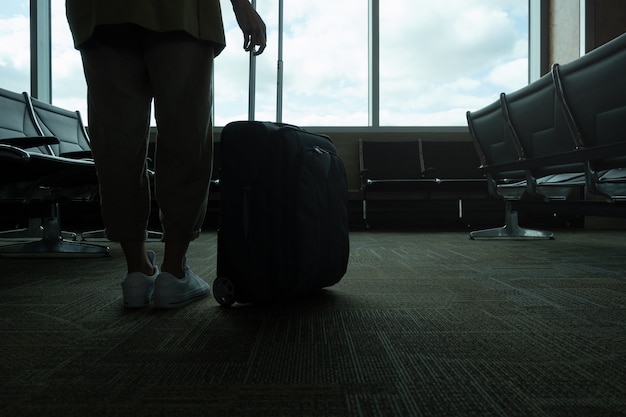 Primer plano horizontal de mujer irreconocible retroiluminada con maleta en el aeropuerto, con espacio de copia.