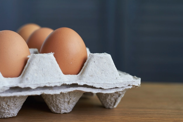 Primer plano de huevos marrones, huevos de gallina en bandeja de cartón sobre mesa de madera