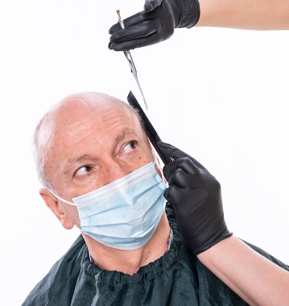 Primer plano de la imagen del hombre mayor en la mascarilla protectora en la peluquería. Peluquero cortando el cabello con tijeras