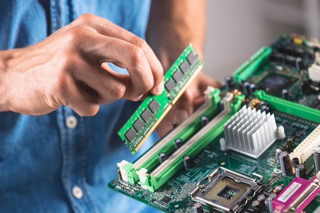 Primer plano de ingeniero poniendo el módulo de memoria RAM en la placa base de la computadora