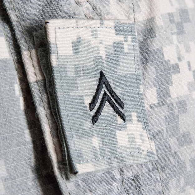 Primer plano de la insignia de rango corporal de soldados del ejército de EE. UU. Bordada en el cuello del uniforme de combate del ejército o parche de solapa en cierre de velcro en tela gris pixelada con patrón de camuflaje universal