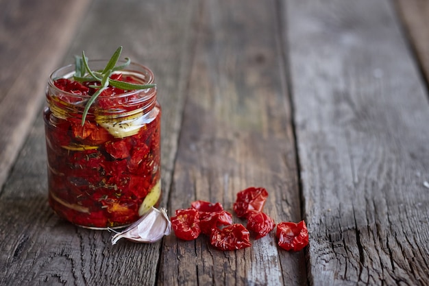 Primer plano de la jarra de tomates caseros secados al sol con hierbas provenzales, ajo y aceite de oliva sobre una superficie de madera rústica, enfoque selectivo