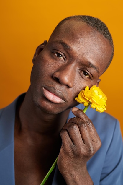 Un primer plano de un joven africano sosteniendo una flor cerca de su cara y mirando una cámara aislada de fondo amarillo