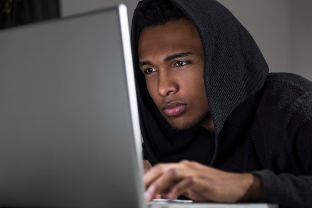 Primer plano de un joven afroamericano codificando en su computadora portátil gris.