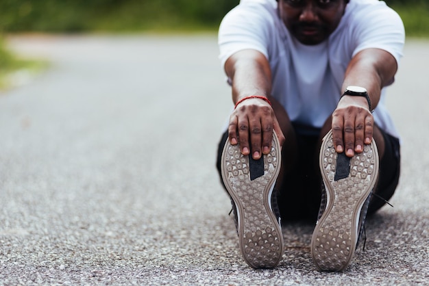 Primer plano Joven atleta asiático corredor deportivo hombre negro usar reloj él sentado tirar de los pies estirando las piernas y la rodilla antes de correr en el parque de salud de la calle al aire libre, ejercicio saludable antes del concepto de entrenamiento