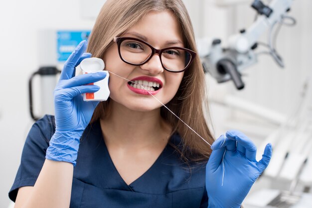 Primer plano de joven y atractiva mujer dentista con hilo dental en la clínica dental