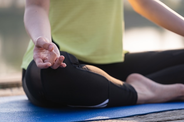 Primer plano de una joven y bella mujer asiática practicando yoga y meditar en la postura del loto al aire libre junto al lago por la mañana para la relajación y la tranquilidad. Concepto de armonía y meditación.