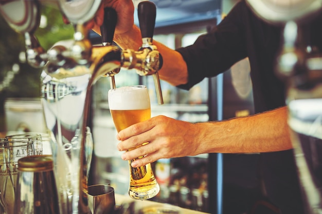 Primer plano de joven camarero vertiendo cerveza mientras está de pie en la barra del bar.