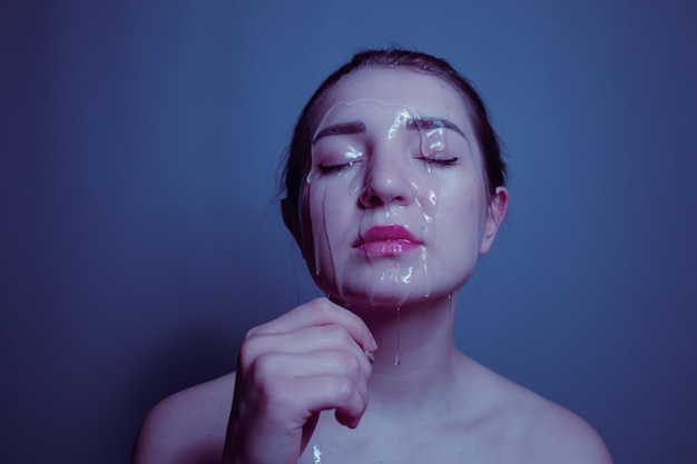 Primer plano de una joven sin camisa con un producto de belleza en la cara contra un fondo azul