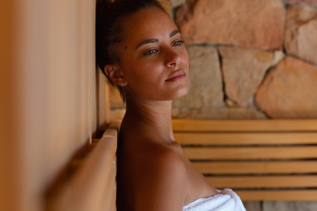 Foto primer plano de una joven caucásica en bata de baño relajándose en la sauna. concepto de spa, bienestar y relajación.