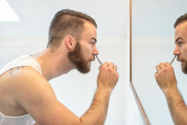 Foto primer plano de un joven cortando la barba reflejándose en el espejo en casa