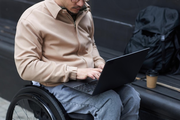 Primer plano de un joven con discapacidad que trabaja en línea en una computadora portátil al aire libre