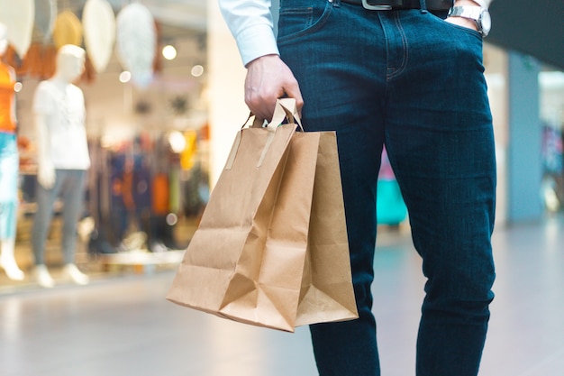 Primer plano de un joven elegante caminando en un centro comercial con bolsas de compras amigables con la ecología en la mano con productos y ropa. Ventas, concepto de descuento agotado. Venta de temporada.