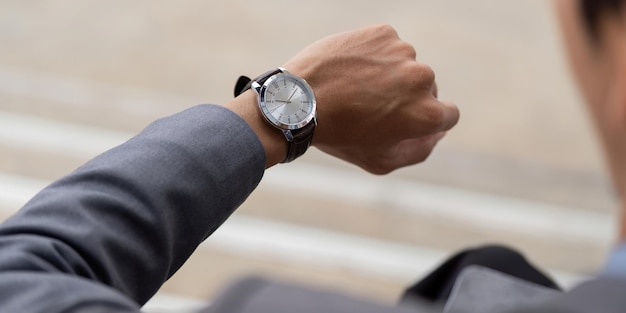Primer plano de un joven empresario asiático comprobando su reloj en un moderno entorno comercial al aire libre
