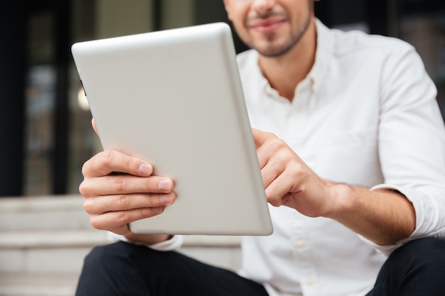 Primer plano de un joven empresario sosteniendo y usando tableta al aire libre