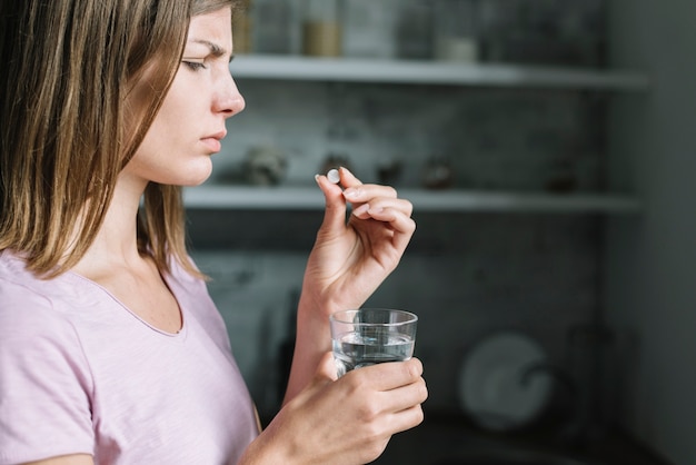 Primer plano de una joven enferma con pastilla y vaso de agua