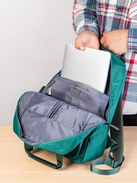 Foto primer plano de un joven estudiante masculino sacando una computadora portátil de una mochila