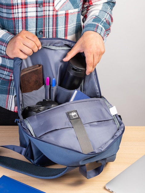 Foto primer plano de un joven estudiante sacando una taza de café de una mochila que también contiene un bloc de notas de billetera portátil