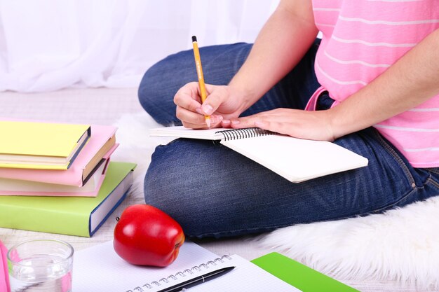 Primer plano de una joven estudiante sentada en el suelo y estudiando sobre un fondo claro