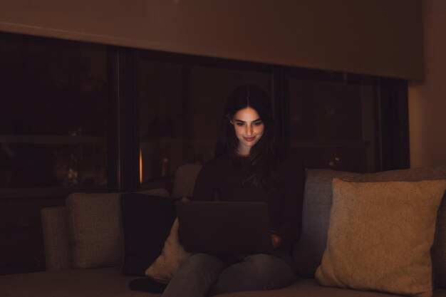 Un primer plano de una joven feliz y alegre mujer sonriendo y usando una computadora portátil en casa sentada en el sofá